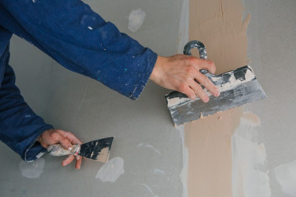 plasterer man works plastering two trowels plasterboard blue uniform 2 1024x682
